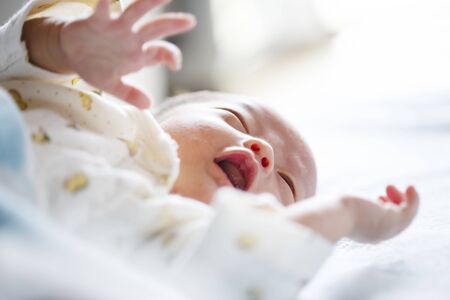 Newborn Concept. child on a white bed. little kid relaxing at home. Newborn baby is fussing and...