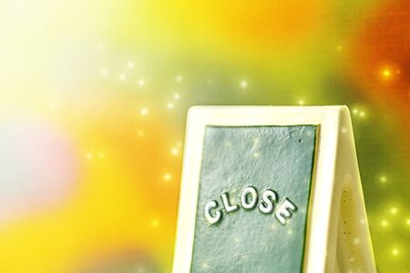 Close up of a green with yellow close chalkboard sign leaning against bright, colorful with sparkly...