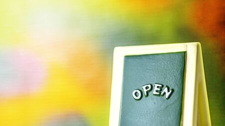 Close up of a green with yellow open chalkboard sign leaning against bright with colorful...