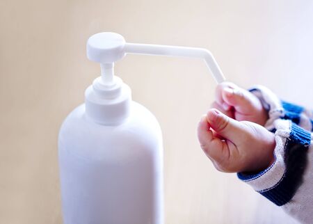 A child sprays her hands with antiseptic from a plastic spray bottle. Hands with a bottle close-up on a blue background. Sanitary treatment during an epidemic.の写真素材