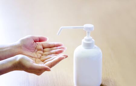 A woman sprays her hands with antiseptic from a plastic spray bottle. Hands with a bottle close-up on a blue background. Sanitary treatment during an epidemic.の写真素材