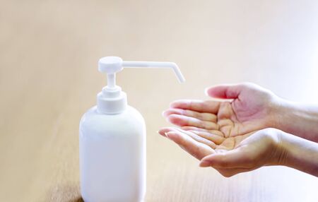 A woman sprays her hands with antiseptic from a plastic spray bottle. Hands with a bottle close-up on a blue background. Sanitary treatment during an epidemic.の写真素材
