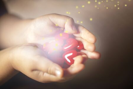 Little child holding red heart to give off light with sparkle, close-up isolated on black gradation and copy space.の写真素材