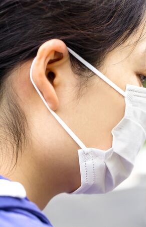 Young woman puts on a medical mask. Symptoms of influenza, fever, pandemic, epidemic. Profile view.の写真素材