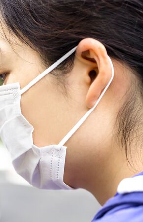 Young woman puts on a simple white air protection mask on the color surface. Symptoms of influenza, fever, pandemic, epidemic. Profile view.の写真素材