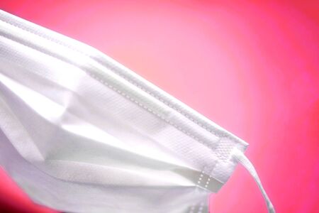 simple white air protection mask on the color surface on pink red background. Disposable surgical face mask cover the mouth and nose. Healthcare and medical concept.の写真素材