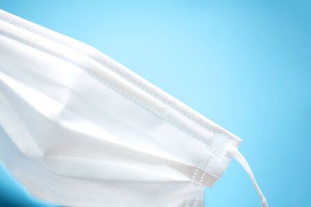 simple white air protection mask on the color surface on blue background. Disposable surgical face mask cover the mouth and nose. Healthcare and medical concept.の写真素材