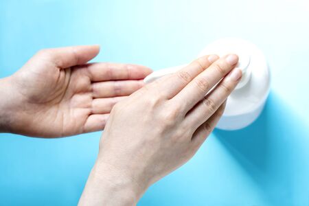 A woman sprays her hand with antiseptic from a plastic spray bottle. Hands with a bottle close-up on a blue background. Sanitary treatment during an epidemic.の写真素材