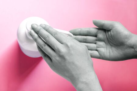 A woman sprays her hand with antiseptic from a plastic spray bottle. Hands with a bottle close-up on a red pink background. Sanitary treatment during an epidemic.の写真素材