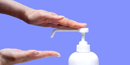 A woman sprays her hand with antiseptic from a plastic spray bottle. Hands with a bottle close-up on a blue purple background. Sanitary treatment during an epidemic.の写真素材