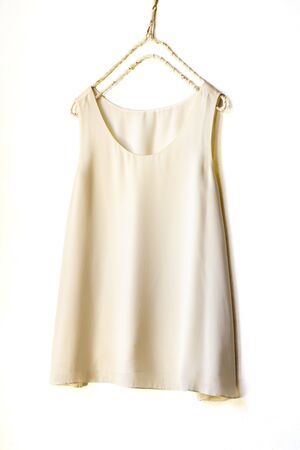 light beige or white tank top hanging on a hanger in a white wall.Close upの写真素材