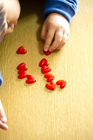 child boy align the lot red hearts motifs on wooden background.boy's hand. copy space.の写真素材