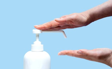 A woman sprays her hand with antiseptic from a plastic spray bottle. Hands with a bottle close-up on a light blue background. Sanitary treatment during an epidemic.の写真素材
