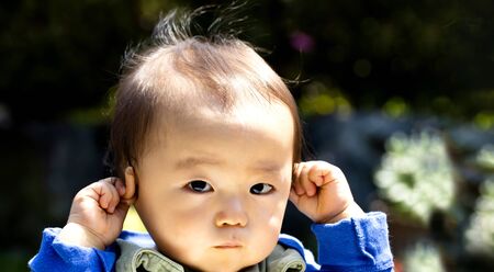 Baby touching his ears isolated on a black background and copy space and outdoors.?or hear no evilの写真素材