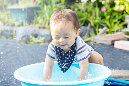 Portrait of happy joyful beautiful little boy isolated on outside background and copy space. boy is dripping wet and plays with water and have a bucket .の写真素材