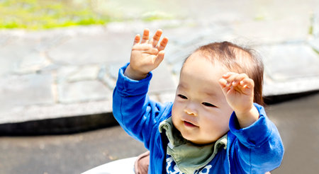 a young kid boy in the garden with both arms in the air. A baby raises both hands.の写真素材