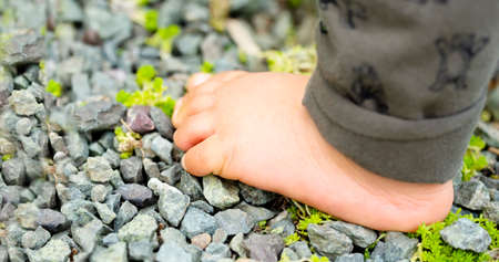 Close up of the one bare foot of the child walking on over gravel and copy space.の写真素材
