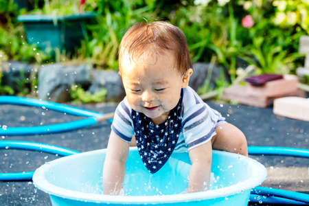 Portrait of happy joyful beautiful little boy isolated on outside background and copy space. boy is dripping wet and plays with water and have a bucket .の写真素材