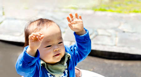 a young kid boy in the garden with both arms in the air. A baby raises both hands.の写真素材