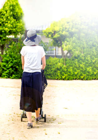 Back figure of young mother pushing her baby in the stroller outside. and copy space.