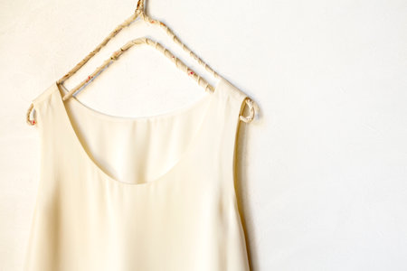 beige or white tank top hanging on a hanger in a white wall. Close up and copy space.の写真素材