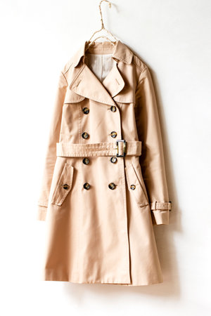 Beige trench coat isolated hanging on a hanger in a white wall. Close up and copy space.の写真素材