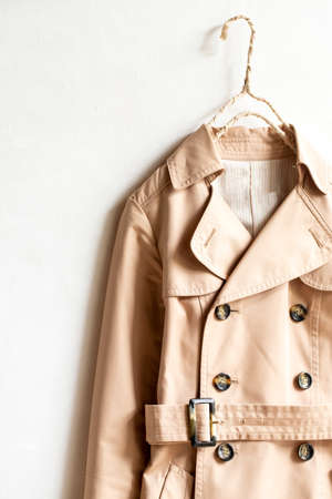 Beige trench coat isolated hanging on a hanger in a white wall. Close up and copy space.の写真素材