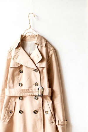 Beige trench coat isolated hanging on a hanger in a white wall. Close up and copy space.の写真素材