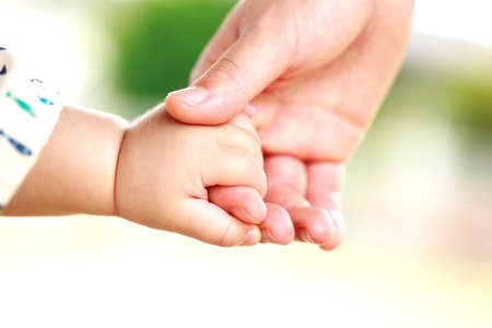 Family scene , close up parent and baby holding hands together and green and whier background with copy space.の写真素材