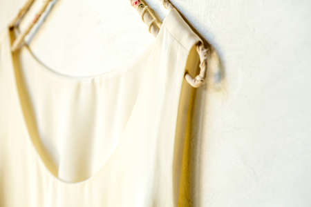 beige or white tank top hanging on a hanger in a white wall. Close up and copy space.の写真素材