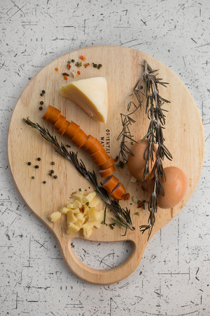 Raw Sausages for grill on wooden board and huge piece of cheese, background of black pepper, eggs and rosemary.. Breakfast in the kitchenの写真素材