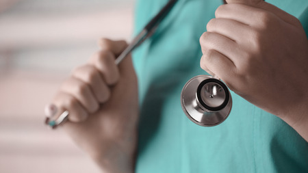 A young female doctor in a blue smock holding a phonendoscope in arms. Blurred background. Concept...