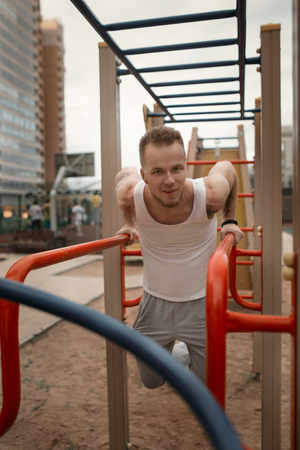 Energetic young man do exercises outdoors in sport square to keep his body in shape. Fitness...
