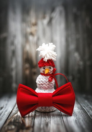 Christmas decoration in vintage toning on dark black wooden background with knitting snowman and red bowtie. Xmas decorative ornaments for design. Art work with texture for holiday new year 2017の写真素材