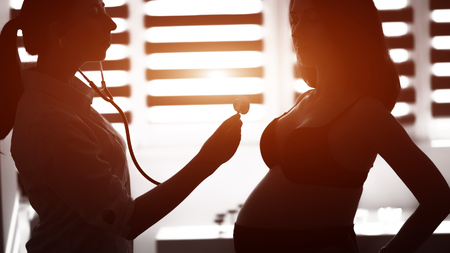 Silhouette female medicine doctor holding stethoscope to pregnant woman standing for encouragement, empathy, cheering,support, medical examination. New life of abortion concept. BW styleの写真素材