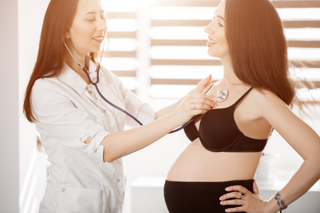 female medicine doctor holding stethoscope to pregnant woman standing for encouragement, empathy, cheering,support, medical examination. New life of abortion concept. Flare for text and designの写真素材