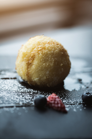 Grilled ice-cream in coconut with sauce and fruits on black stone plate in front of window. Asian food background. Eating concept. Restaraunt place with wooden table. Flare Copy space for text, designの写真素材