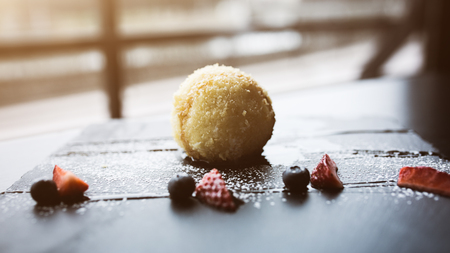 Grilled ice-cream in coconut with sauce and fruits on black stone plate in front of window.Asian food background. Eating concept. Restaraunt place with wooden table. Flare Copy space for text, designの写真素材