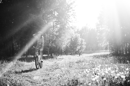 Funny girl driving bicycle outdoor. Sunny summer lifestyle concept. Woman in dress and hat in Field with dandelions. Female ride in park. Light effect for text. Copyspace for design. BW photoの写真素材