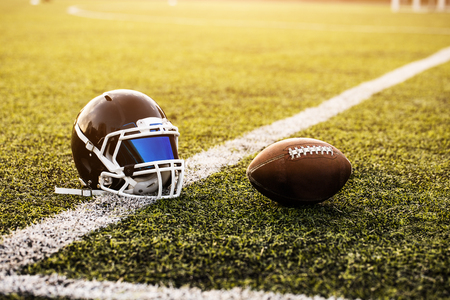 American Football Helmet and ball on green grass pattern for football sport, Football field, soccer field, team sport texture. White stripe on it. Close up focus. Flare sunlight for text and designの写真素材
