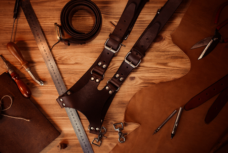 Leather craft and belt for photographers. Tanners tools on grey wooden background top view.