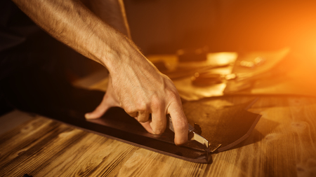 Working process of the leather belt in the leather workshop. Man holding tool. Tanner in old...