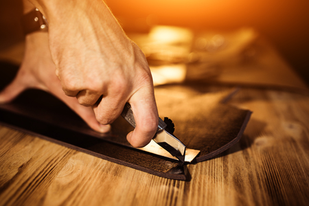Working process of the leather belt in the leather workshop. Man holding tool. Tanner in old...