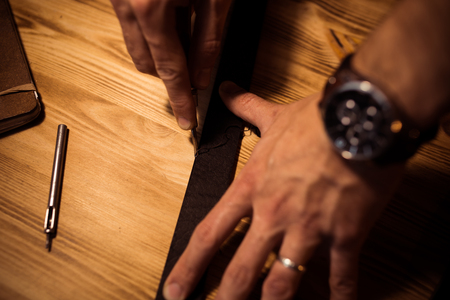 Working process of the leather belt in the leather workshop. Man holding crafting tool and working....