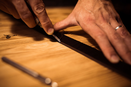 Working process of the leather belt in the leather workshop. Man holding crafting tool and working. Tanner in old tannery. Wooden table background. Close up man arm.の写真素材