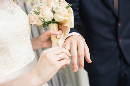 Big nice wedding bouquet in womans hands. The bride puts the ring on the grooms finger.の写真素材