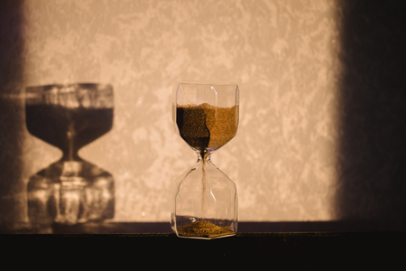 Hourglass with shadow on wall. Time passing concept for business deadline, urgency and running out...