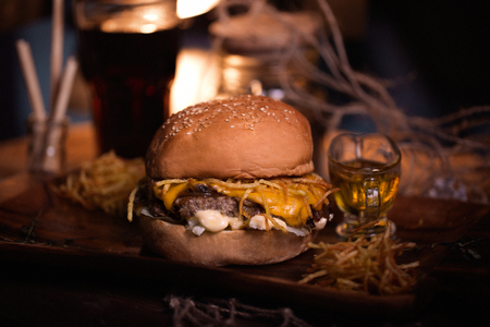 Burger food photo. Street food. Fresh tasty grilled beef hamburger cooked at barbecue on wooden table. Big cheeseburger with steak meat closeup with unfocused background. Rustic color style.の写真素材