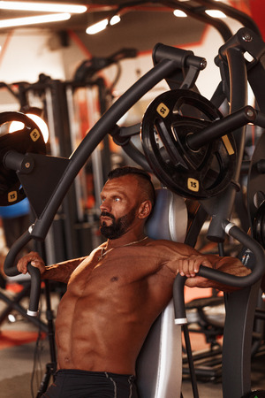 Chest press. Handsome muscular sexy man in gym doing exercises. Tanned athlete. Chest workoutsの写真素材