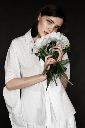 Portrait of a beautiful girl with peonies. Beauty retouching photo. Fashion and cosmetic concept. Grey studio background.の写真素材